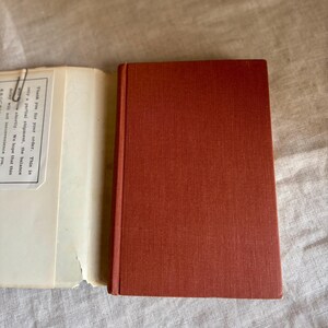 May include: A closed, rectangular, rust-colored book with a textured cover sits next to an open book with off-white pages. The open book has text that reads "Thank you for your order. This is only a partial shipment, the balance will follow shortly. We hope that this delay will not inconvenience you."