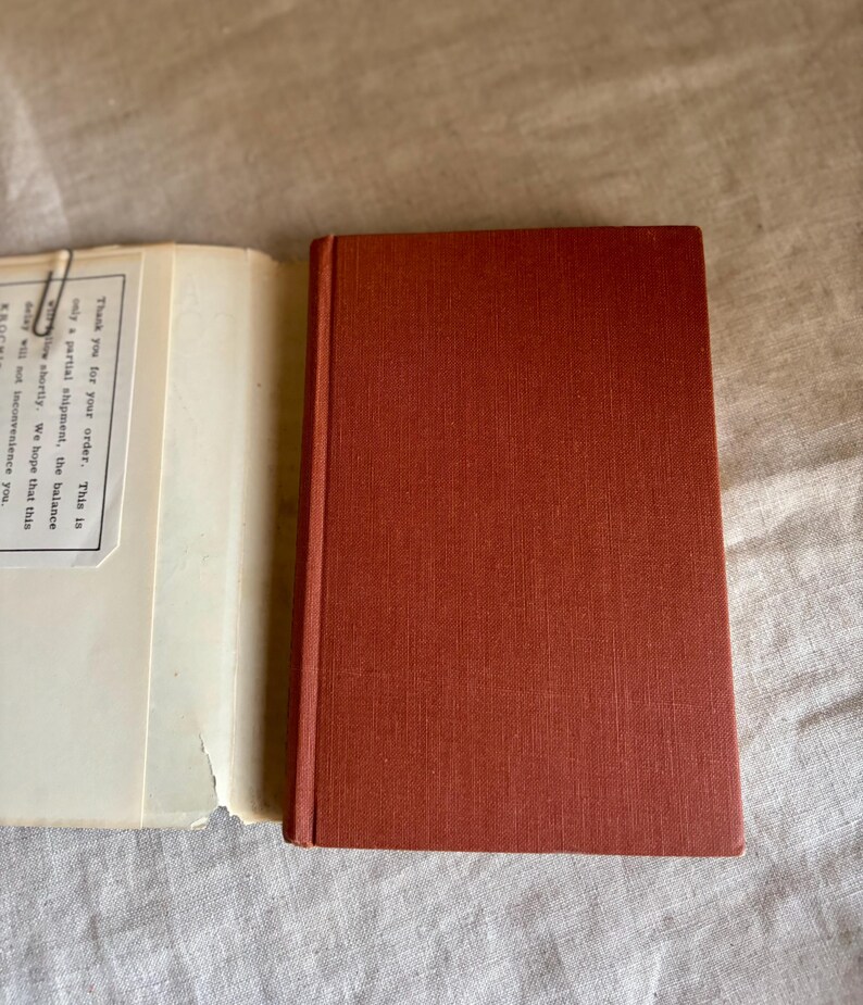 May include: A closed, rectangular, rust-colored book with a textured cover sits next to an open book with off-white pages. The open book has text that reads "Thank you for your order. This is only a partial shipment, the balance will follow shortly. We hope that this delay will not inconvenience you."