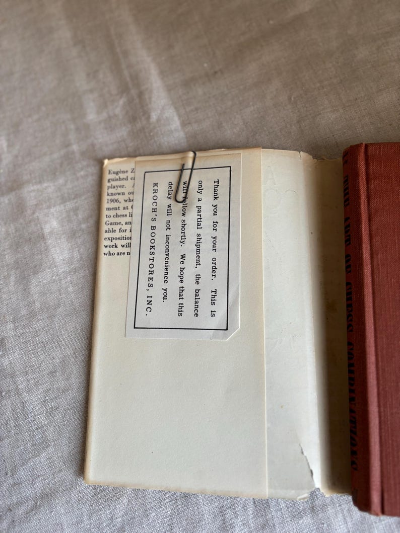 May include: An open book with a red cover and a white paper insert held in place by a paper clip. The insert has text that reads "Thank you for your order..." and "KROCH'S BOOKSTORES, INC."