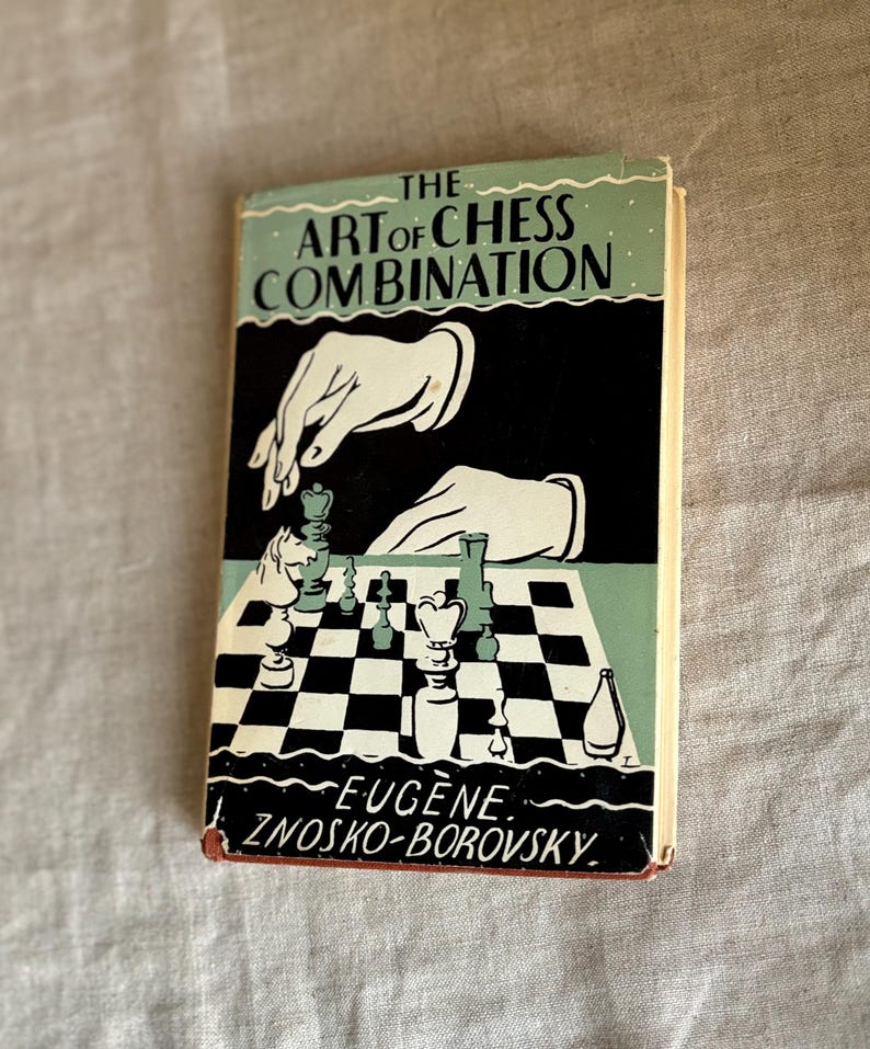 May include: Vintage book titled "The Art of Chess Combination" by Eugene Znosko-Borovsky. The cover features a black and white illustration of chess pieces on a checkered board, with hands reaching down. The book has a light blue and black color scheme.