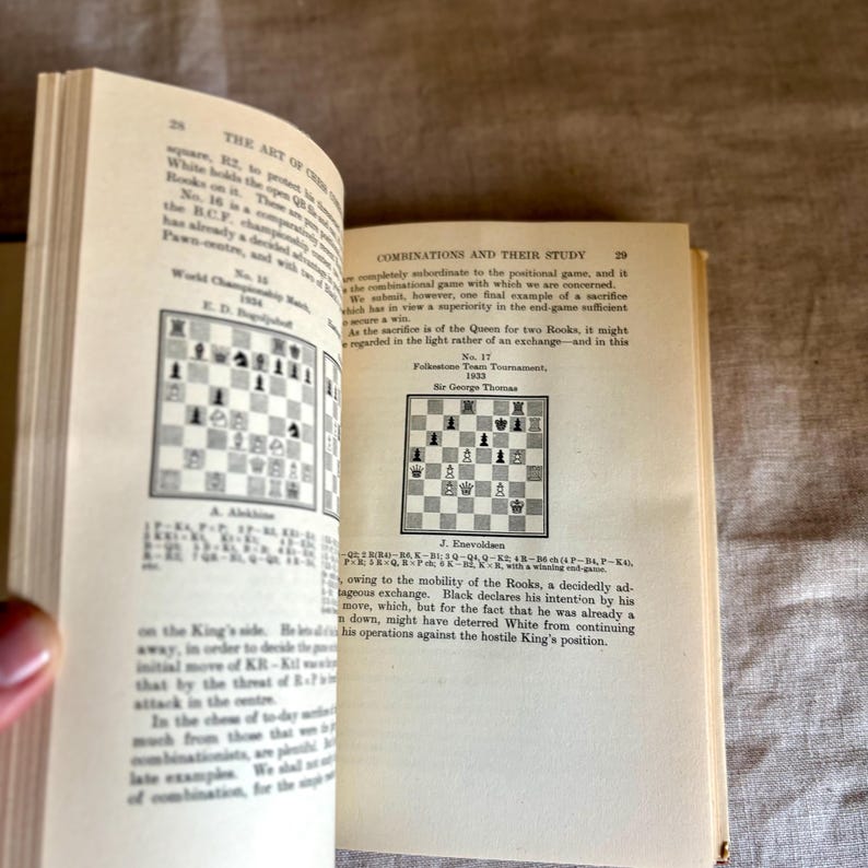 May include: Open book with text and chess diagrams. The pages are aged, with text titled "THE ART OF COMBINATIONS" and "COMBINATIONS AND THEIR STUDY". Chess diagrams illustrate game positions. The book is open, revealing the content.