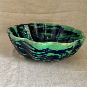 May include: A ceramic bowl with a scalloped rim, featuring a vibrant green and navy blue wave pattern. The bowl's exterior has a textured appearance, and the rim shows signs of wear.