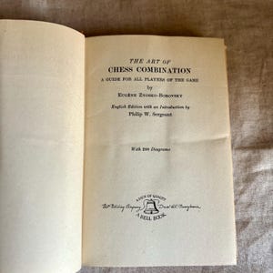 May include: Open book titled "THE ART OF CHESS COMBINATION" by Eug&egrave;ne Znosko-Borovsky. The book is an English edition with an introduction by Philip W. Sergeant. The book cover is off-white with black text. The book is a guide for all players of the game.