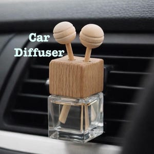 May include: A car air freshener with a wooden top and two spherical wooden diffusers. The air freshener sits in a clear glass bottle. The text "Car Diffuser" is visible in the image.