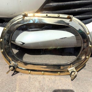 Puede incluir: Ojo de buey ovalado de latón con una ventana de vidrio transparente. El ojo de buey tiene un acabado pulido y está asegurado con múltiples remaches y dos mecanismos de cierre. Un artículo decorativo de temática náutica.