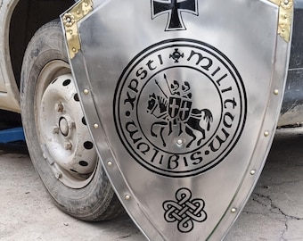 Può includere: Uno scudo color argento con una croce nera e un emblema circolare con cavalieri a cavallo. Lo scudo ha dettagli dorati agli angoli ed è probabilmente in metallo.