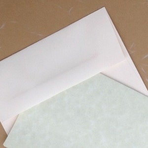 K&ouml;nnte beinhalten: Ein cremefarbener Umschlag, der teilweise ge&ouml;ffnet ist und ein hellgr&uuml;nes Schreibwarenblatt freigibt. Die Schreibwaren haben ein subtiles, strukturiertes Muster. Der Hintergrund ist hellbraun mit wei&szlig;en Flecken, was eine neutrale und elegante &Auml;sthetik erzeugt. Ideal f&uuml;r Schreibwaren.