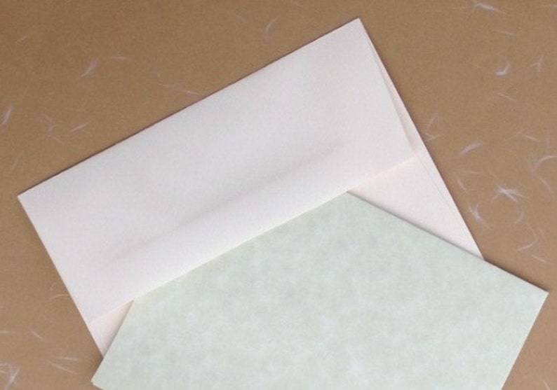 K&ouml;nnte beinhalten: Ein cremefarbener Umschlag, der teilweise ge&ouml;ffnet ist und ein hellgr&uuml;nes Schreibwarenblatt freigibt. Die Schreibwaren haben ein subtiles, strukturiertes Muster. Der Hintergrund ist hellbraun mit wei&szlig;en Flecken, was eine neutrale und elegante &Auml;sthetik erzeugt. Ideal f&uuml;r Schreibwaren.