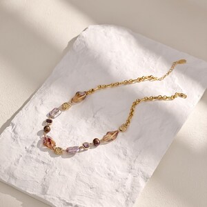 May include: A gold-toned necklace with a variety of beads in shades of brown, purple, and clear. The necklace features a delicate chain and decorative gold accents. The beads have an irregular shape, adding to the necklace's unique design.