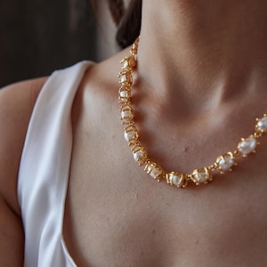 May include: A gold-colored necklace featuring irregularly shaped pearls. The pearls are encased in a gold metal setting, creating a unique and elegant design. The necklace is worn around the neck.