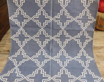May include: A blue and white patterned rug with a geometric design. The rug features a repeating pattern of white shapes on a blue background. The rug has a fringe along the bottom edge.