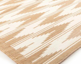 Puede incluir: Alfombra beige y blanca con diseño geométrico. La alfombra presenta un patrón repetitivo de líneas diagonales en color beige claro sobre un fondo blanco. La alfombra tiene una textura tejida y un borde beige.