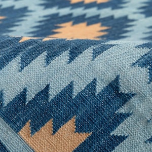 Könnte beinhalten: Nahaufnahme eines gewebten Teppichs mit geometrischem Muster. Der Teppich weist ein sich wiederholendes Design aus blauen und beigen Formen auf hellem blauem Hintergrund auf. Die Textur des Teppichs ist sichtbar, was auf eine handgefertigte oder handwerkliche Qualität hindeutet.