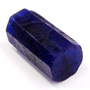 Peut inclure: Une pierre précieuse bleu foncé facettée de forme hexagonale. La gemme a une surface polie et réfléchissante et une couleur riche et saturée. La pierre est d'un bleu royal profond, avec de subtiles variations de tons.