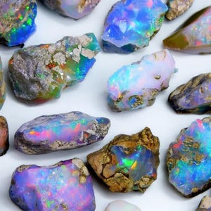 May include: A collection of raw, unpolished opal stones featuring irregular shapes and rough, earthy textures. The stones display vibrant flashes of iridescent blue, green, and pink light against a translucent to opaque base with rocky inclusions.