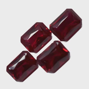 Può includere: Quattro pietre preziose rettangolari, sfaccettate, rosso intenso, sono esposte su uno sfondo bianco. Le gemme hanno un colore ricco e saturo e un alto grado di chiarezza, con bordi netti e un aspetto lucido. Le gemme sono disposte ad angoli.