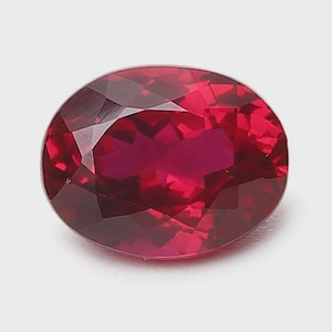 Könnte beinhalten: Ein facettierter, ovalförmiger Rubin-Edelstein. Der Edelstein hat eine tiefe, satte rote Farbe mit inneren Reflexionen. Der Schliff des Steins erzeugt mehrere Facetten, die das Licht reflektieren.