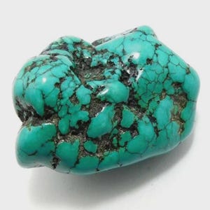 Puede incluir: Una piedra preciosa de turquesa en bruto, de color turquesa vibrante con vetas oscuras. La piedra tiene una forma irregular y una superficie pulida y brillante. Un hermoso ejemplo de turquesa natural.