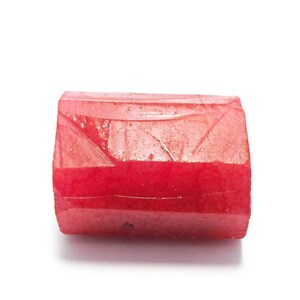 Puede incluir: Una gema roja rectangular con una superficie texturizada. La gema tiene una apariencia en capas con una banda roja más oscura en el medio. Los bordes son ligeramente redondeados.