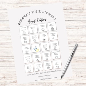 May include: A white paper titled "Workplace Positivity Bingo August Edition" with a grid of squares, each with a different task. A silver pen rests on the right side of the paper. The text "Instant Motivation, Daily Acts of Kindness, Team Spirit" is at the bottom.