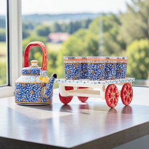 May include: A blue and white floral patterned ceramic teapot with a red handle and a matching set of glasses on a decorative cart with red wheels. The teapot and glasses are on a grey countertop.
