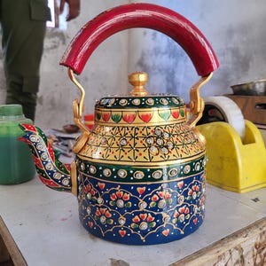 May include: An ornate, hand-painted teapot with a red handle and gold accents. The blue body is decorated with floral patterns and rhinestones. The spout and lid are also adorned with intricate designs. A decorative kitchenware item.
