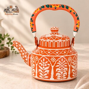 May include: A bright orange metal teapot featuring intricate white floral and arch patterns across the body and lid. The curved handle is decorated with painted yellow and green flowers, while the spout displays a white polka dot design.
