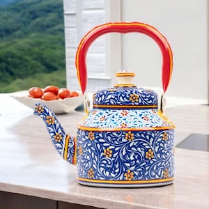 May include: A decorative blue and white floral patterned teapot with a red handle and spout. The teapot has yellow accents and a matching lid. The teapot is sitting on a countertop.