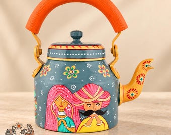 May include: A teal metal teapot featuring a hand-painted design of a person in a pink head covering and a person in a yellow turban with a mustache. The teapot has an orange arched handle, a yellow spout with floral motifs, and white dots.