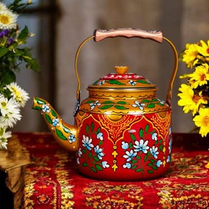 May include: A red and gold hand-painted teapot with a floral design. The teapot features a wooden handle and a curved spout. The design includes blue and white flowers and green leaves. The teapot is sitting on a red patterned tablecloth.