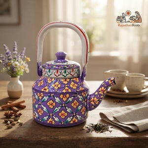 May include: A purple metal teapot featuring a hand-painted floral pattern in yellow, white, and green. The teapot has a curved handle, a matching lid, and a spout. The surface is decorated with a repeating geometric motif and the RajasthanRoots logo.