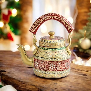 May include: Ornate, gold-colored teapot with a red handle and intricate floral and jewel detailing. The teapot features a decorative design with red, green, and gold accents. The teapot is sitting on a wooden surface.