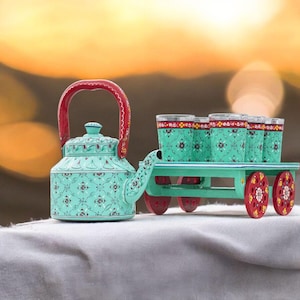 May include: A teal teapot with a red handle and floral pattern, beside a small green cart carrying six teal glasses. The cart has red and white wheels. The scene is set against a blurred, warm-toned background.