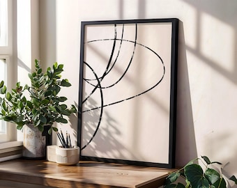 May include: A framed abstract art print with black lines on a beige background. The artwork is displayed on a wooden surface next to a potted plant and a pencil holder. The frame is black.