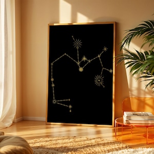 May include: A framed black art print featuring a gold constellation design. The artwork is displayed in a room with natural light, a plant, and a modern orange side table. The constellation art is a decorative piece.