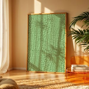 May include: A framed artwork featuring a green, textured pattern reminiscent of reptile skin. The artwork is displayed in a well-lit room with a wooden floor, a plant, and a modern orange table.