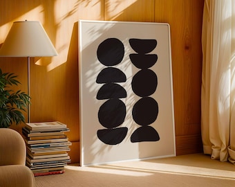 Puede incluir: Impresión artística enmarcada con formas geométricas negras sobre fondo crema. La obra de arte se muestra en un marco blanco y se apoya en una pared de madera. La habitación también incluye una lámpara, libros y una silla.