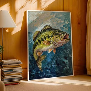 May include: An oil painting of a largemouth bass, featuring a green and yellow fish with orange fins against a textured blue and white backdrop. The artwork is framed in white and displayed in a room with natural light, next to a stack of books.