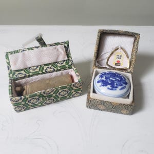 May include: Two antique Chinese stamp sets. One set features a rectangular stone stamp in a green and white patterned box. The other set has a blue and white porcelain stamp with a dragon design in a decorative box with a tag.