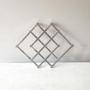 May include: A silver-colored metal wine rack with a diamond-shaped design. The rack is made of thin, intersecting bars, creating multiple compartments for storing wine bottles. The rack is designed to hold multiple bottles.