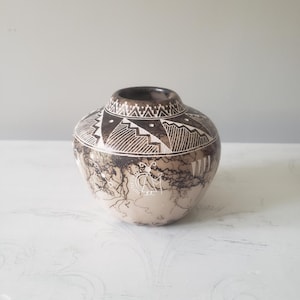 May include: A handcrafted, round pottery vase with a dark brown rim and a beige body. The vase features intricate white geometric patterns and a unique, lightning-like design. The pottery is a decorative piece.