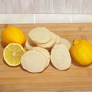 May include: A wooden cutting board with sliced cookies and lemons. The cookies are light beige and round, and the lemons are bright yellow. One lemon is sliced in half, revealing the interior.