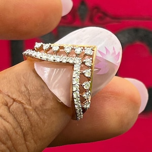 May include: A V-shaped gold ring featuring a double row of small, clear, round-cut stones set along the top and side edges. The band has an open, airy design with a series of vertical metal prongs connecting the two rows of sparkling stones.