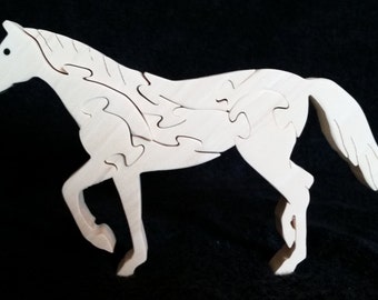 May include: A light-colored wooden horse puzzle consisting of several interlocking pieces. The horse is depicted in a standing position with one front leg raised, featuring a smooth finish and visible wood grain throughout the entire structure.