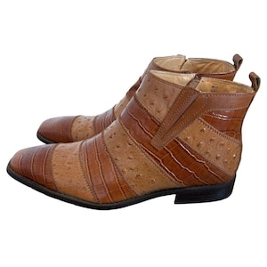 May include: A pair of brown ankle boots featuring a multi-textured design with alternating panels of smooth ostrich-embossed leather and crocodile-embossed leather. The boots have a square toe, a side zipper closure, and a low stacked heel.