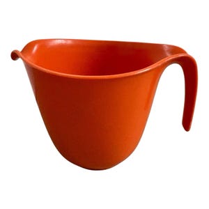 Peut inclure: Un saladier en plastique orange avec une poignée. Le bol a une forme incurvée et une surface lisse. La poignée est une extension incurvée du bord du bol. Le bol est vide et se trouve sur un fond blanc.