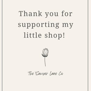 May include: A cream-colored card with the text "Thank you for supporting my little shop!" in a serif font. Below the text is a simple line drawing of a flower and the words "The Sawyer Lane Co."
