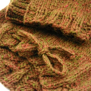 May include: A close-up of a knitted fabric with a green and red color scheme. The fabric is textured and has a loose weave. The fabric is folded over itself, creating a layered effect.