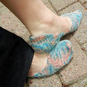 May include: A pair of blue and pink patterned socks with a lacy knit design. The socks are worn on a person's feet.