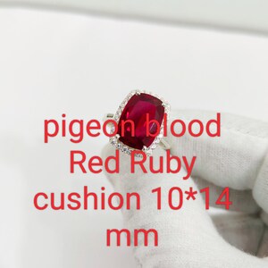 Puede incluir: Anillo de plata con un rub&iacute; rojo de talla coj&iacute;n, rodeado de peque&ntilde;as piedras transparentes. El texto en la imagen dice: "pigeon blood Red Ruby cushion 10*14 mm". El rub&iacute; mide 10 mm x 14 mm.